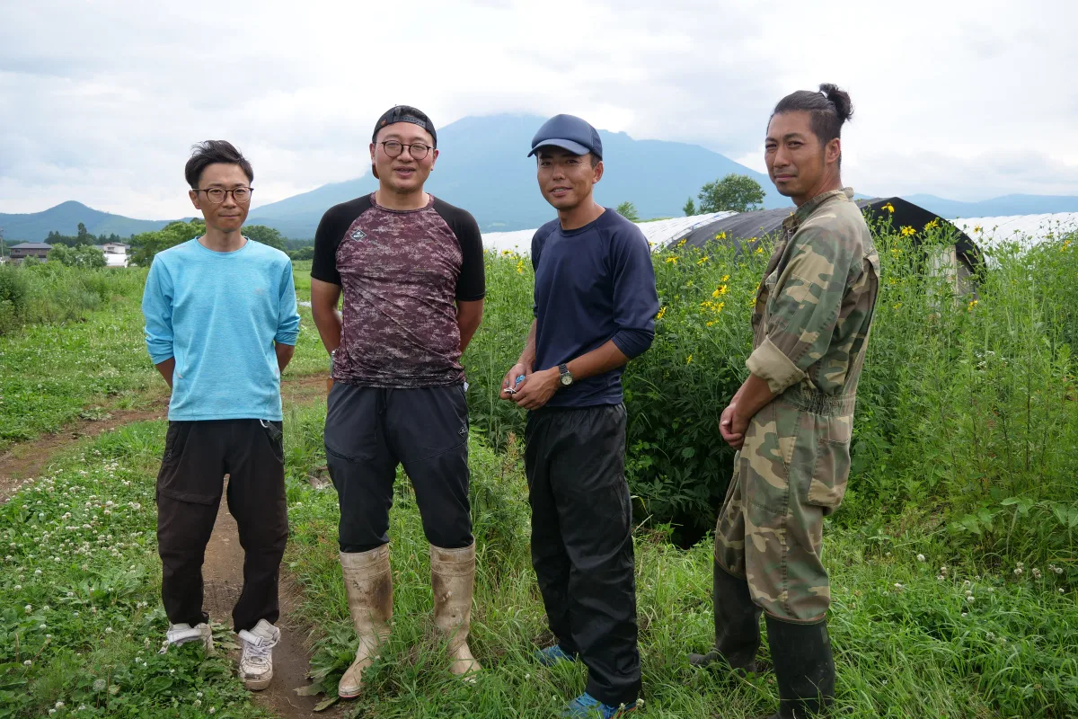 山と畑を背景に並ぶ4人のスタッフ