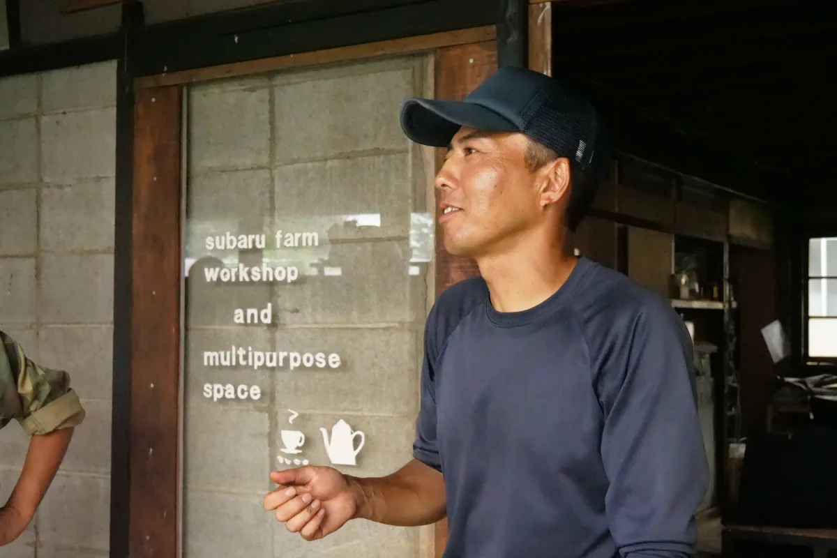 作業場で手を動かしながら話す帽子をかぶったスタッフ