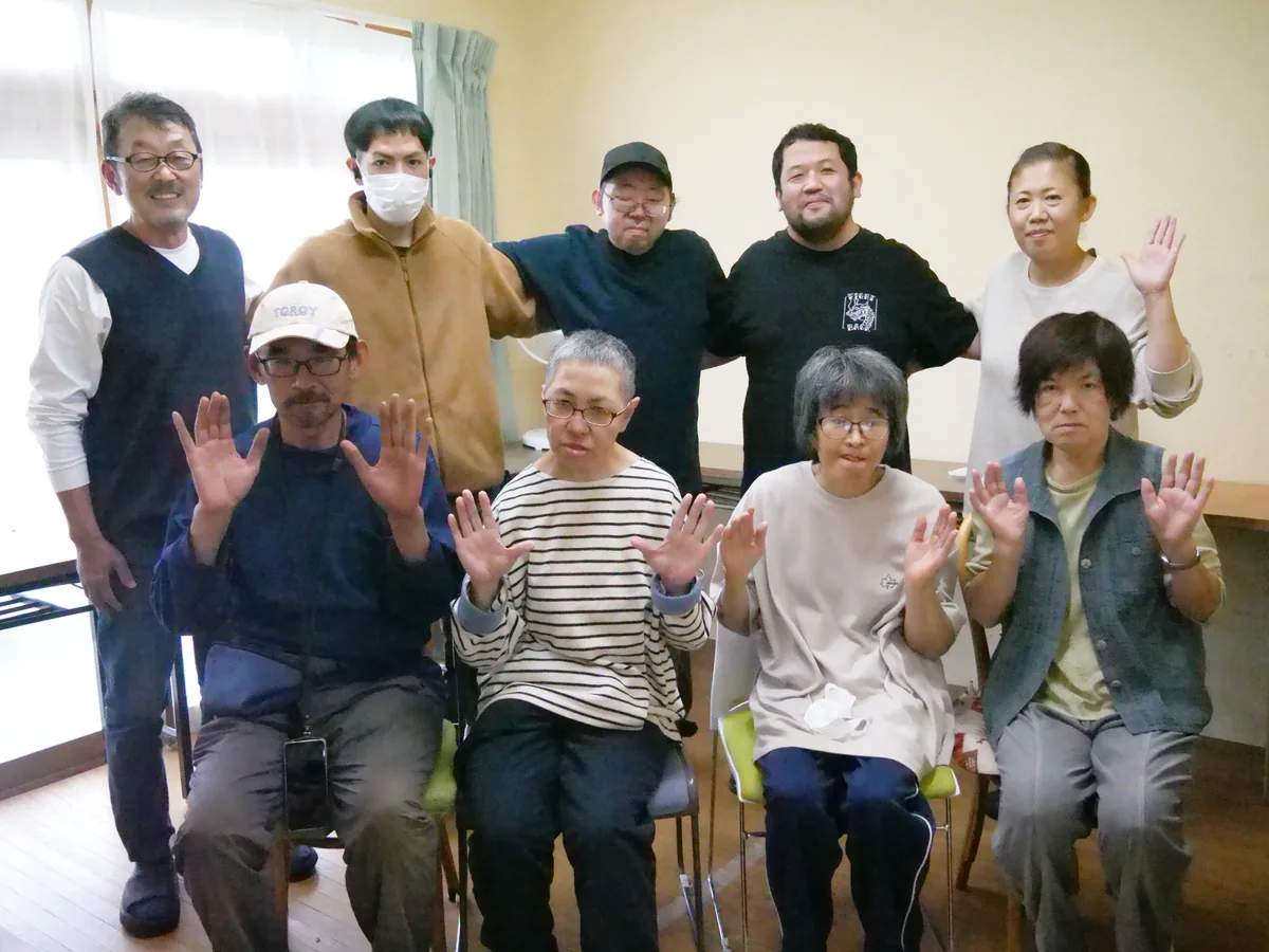 室内で並び、カメラに向かって手を上げる人たちの集合写真