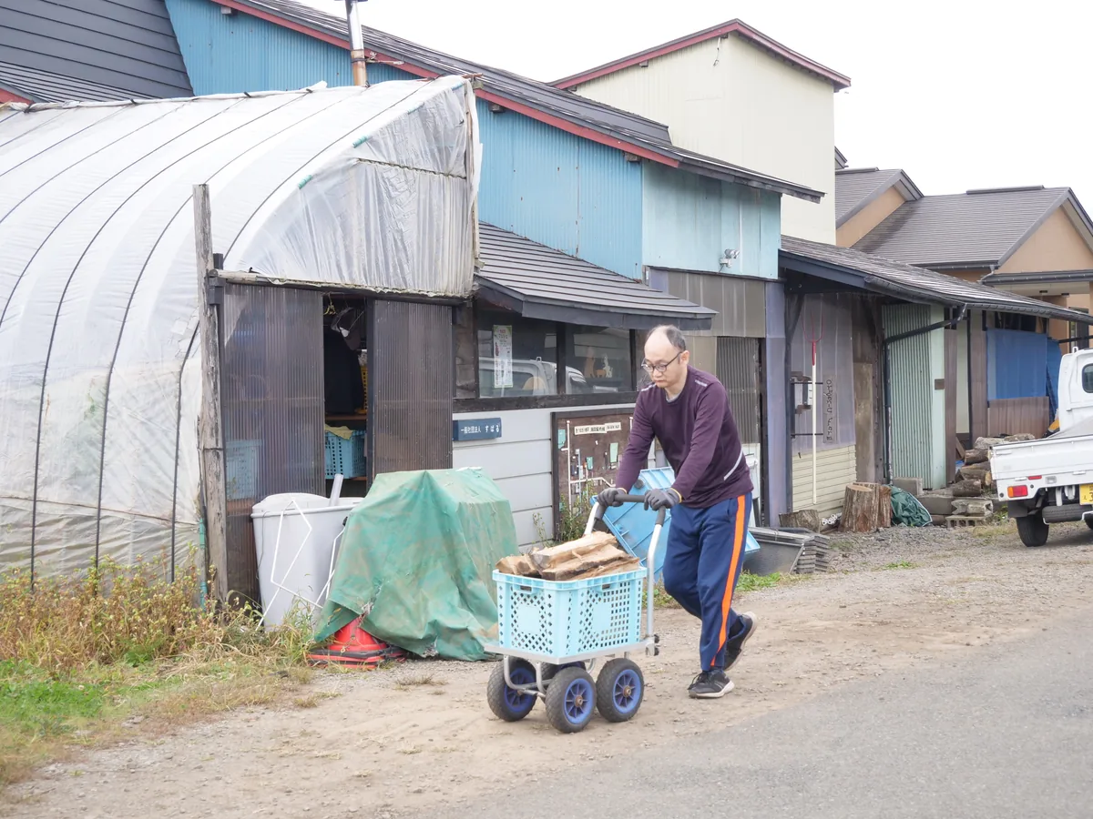作業場の前で、薪の入った水色のかごを載せた台車を押す人