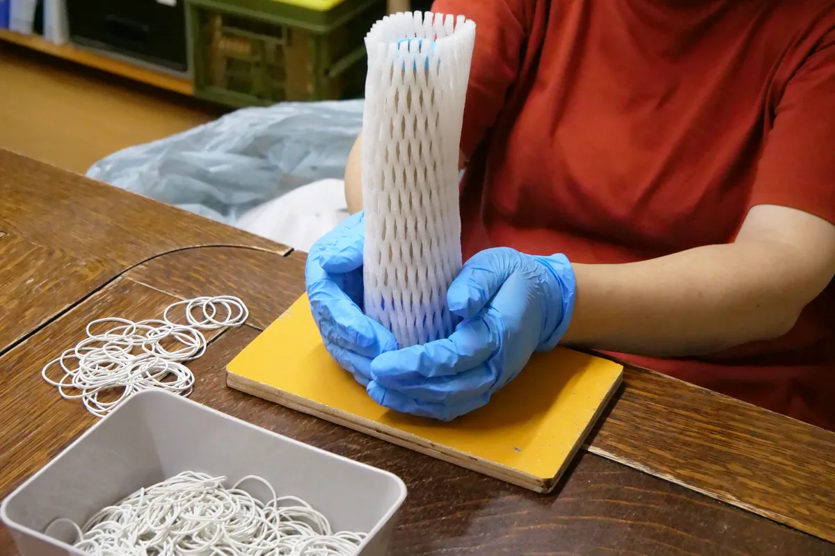 筒に白い緩衝材を重ねる青い手袋の両手