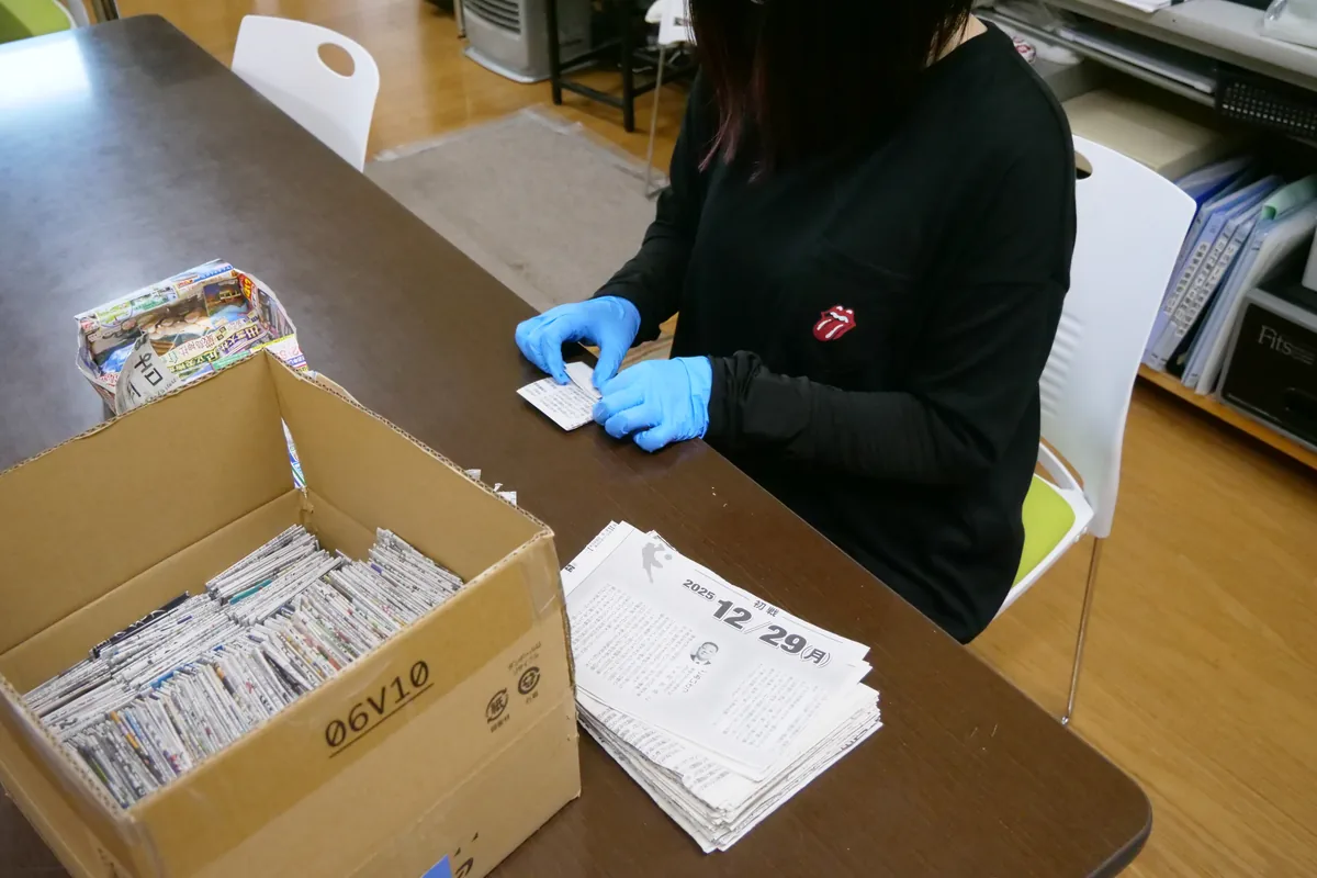 青い手袋をつけ、作業台で紙を折り込む手元