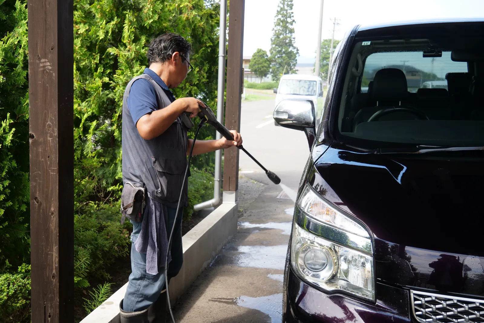 屋外で黒い車へ高圧洗浄機の水をかける人物