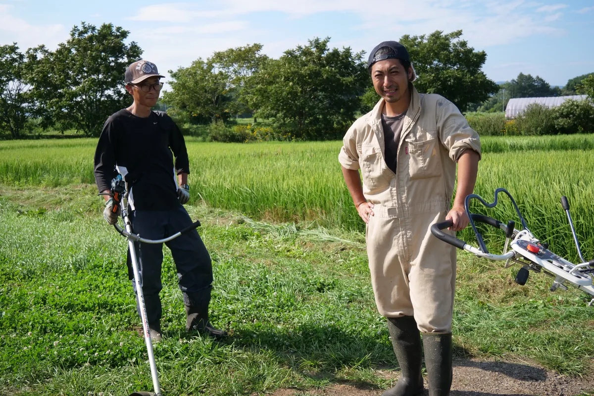 草刈りの道具を手に、田んぼのそばに立つ二人