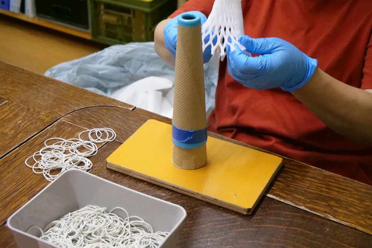 青い手袋で白い緩衝材を筒に重ねる手元
