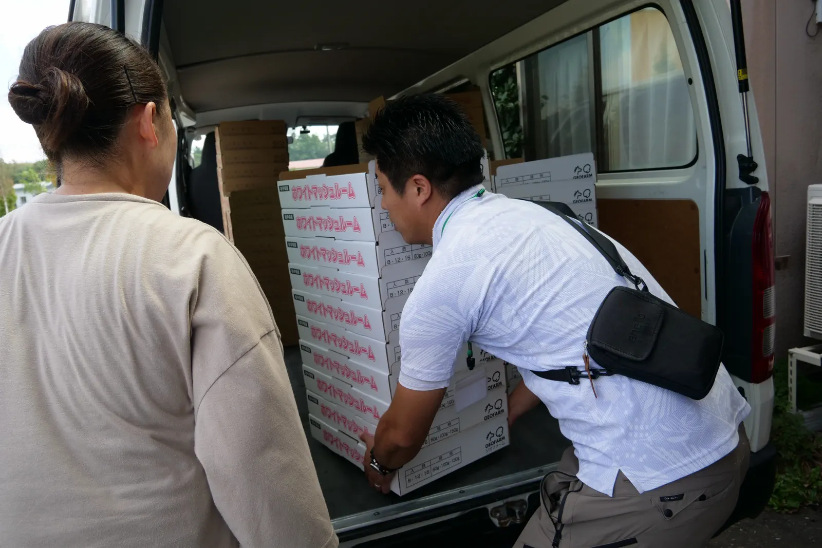 白い車両の荷室で荷物を整える人物